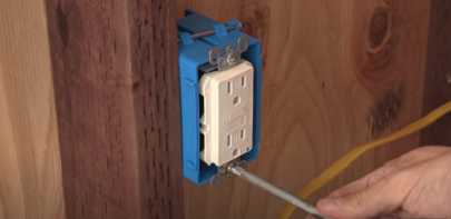 Electrician installing residential GFCI outlet with screwdriver.